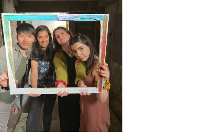 Four actors pose looking through wooden frame