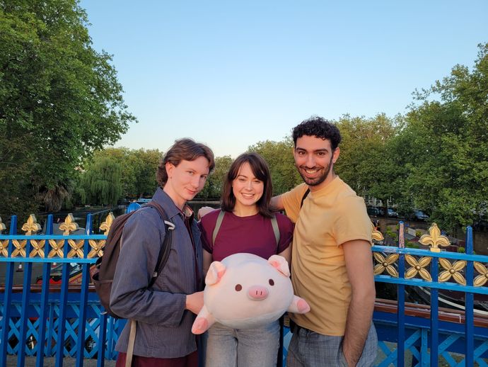 Three people standing on a bridge, posing for the camera with a toy pig