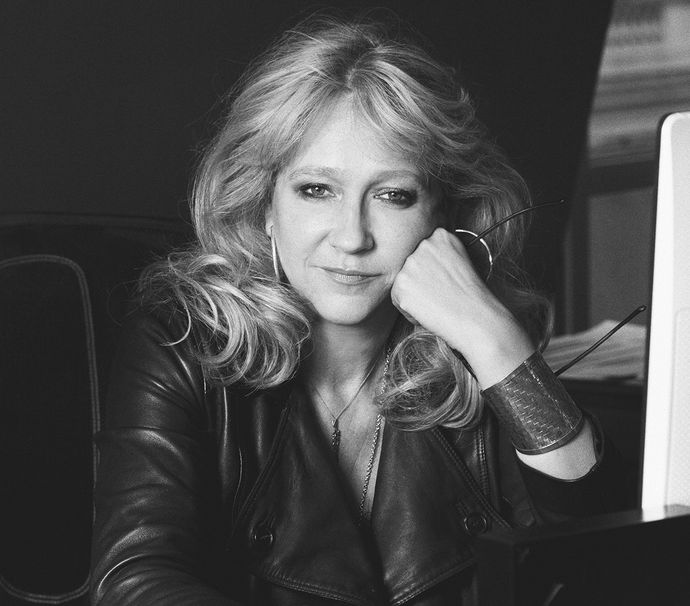 Sonia Friedman OBE headshot in black and white showing Sonia wearing a black jacket with her hair down, standing against a black background, looking into the camera