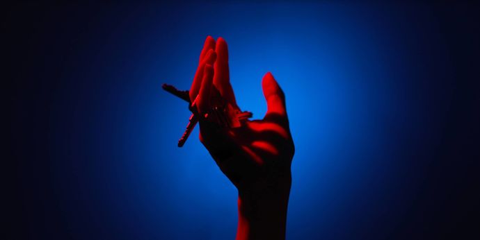 An open hand is in the centre of frame, in between the fingers are keys. The hand is bright red and the background of the image is blue. There is a vignette effect around the edge, making the image focused on the centre of frame. 